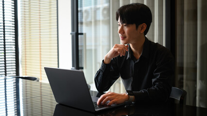 A contemplative Asian businessman focusing on remote work in a bright, modern space
