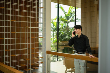 A Confident Young Asian Businessman using a smartphone during a casual conversation, standing in a...