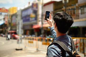 A Young traveler lifts his phone to take a photo of the lively cityscape during a sunny sightseeing...