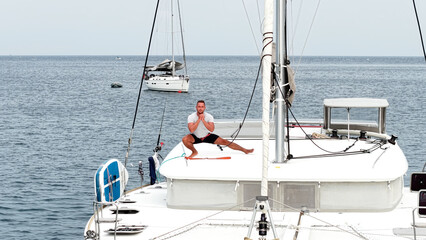 Morning on a yacht. Fitness exercises on the roof of a catamaran. A man doing exercises during a...