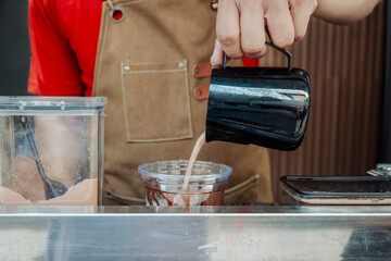 Barista completes the iced chocolate drink by pouring remaining chocolate mixture from a black...