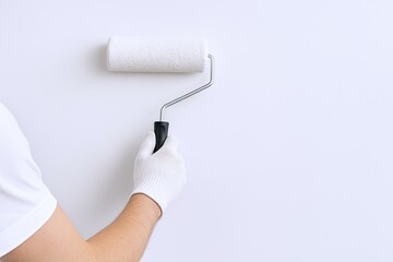 Obraz premium Hand holding paint roller with white textured surface and black handle on white wall.