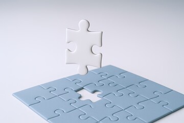 Empty light blue jigsaw puzzle with one piece floating above on a plain white background.