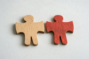 Fototapeta premium Two wooden figures, one natural and one red, symbolize diversity and connection, highlighting individuality within unity.