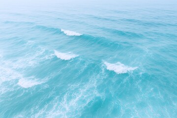 Aerial view of calm turquoise ocean waves gently crashing on a clear bright day.