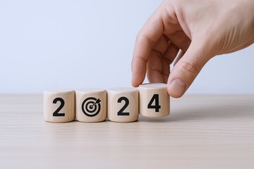 Hand arranging wooden blocks with the numbers 2024 on a light surface for New Year celebration.