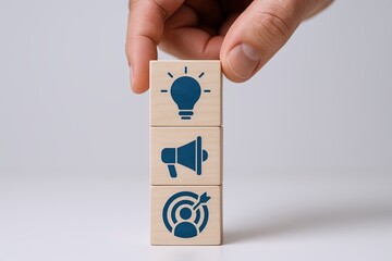 Hand placing wooden blocks with light bulb megaphone and target icons on gray background.