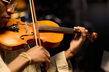 Black man playing violin with focused expression, close up on hands and instrument, adult musician...