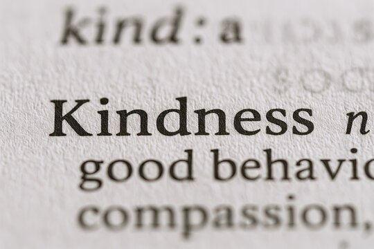 Close-up of the word kindness highlighted in black bold font on dictionary page showing its definition and related words.