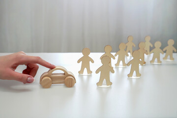 A hand moves a wooden car to a group of wooden figures of people. car duties