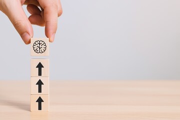 Hand stacking wooden blocks with arrows and brain symbol on top for education.