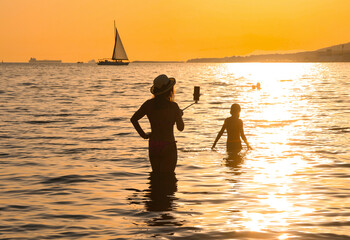 young mother in swimsuit taking selfie in sea at beautiful sunset on summer evening. Silhouette