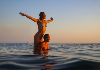 Young couple lovers swimming in sea at beautiful sunset on summer evening.