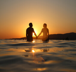 Young couple lovers  enters sea at beautiful sunset on summer evening.