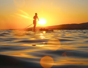 young man  riding  on sup surfing in the sea at sunset.