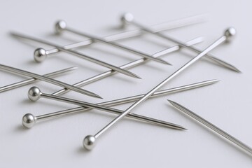 Fototapeta premium Close-up of multiple silver sewing pins with rounded heads scattered on white surface.