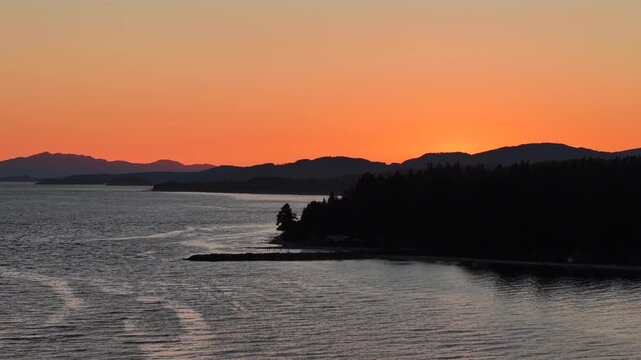 A sunset on the Sunshine Coast with a rocky point and layers of mountains in the distance. The ocean meets the deep oranges of the sky,