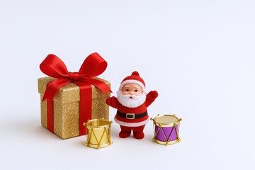 Cute Santa Claus figure with a large gold gift box adorned with a red ribbon and bows, flanked by two colorful drums, festive holiday decoration scene.