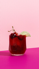 Red sleepy girl mocktail with cherries and lime on striped pink backdrop. Concept of non-alcoholic...