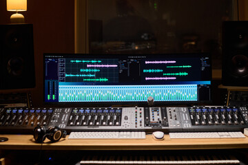 Professional audio mixing console with large digital display showing multitrack waveforms and sound...