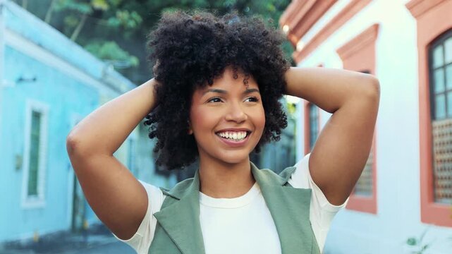 Confident young Black woman smiling while touching her natural curly hair. Beauty, self-love and authenticity in a colorful urban setting.