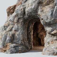 Entrance to a rugged textured cave carved into a weathered rock formation with a sandy floor and sparse vegetation