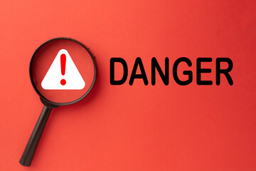Danger and safety warning concept. A magnifying glass with an exclamation mark icon over the word...