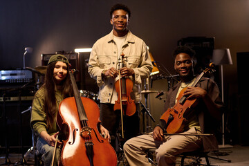 Multiethnic group of young adult musicians posing with string instruments in music studio, Latin...
