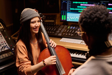 Young adult Hispanic woman smiling while playing cello in music studio, interacting with young...