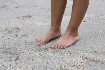 Barefoot child’s feet standing on soft beach sand, capturing a tender and natural moment by the seaside