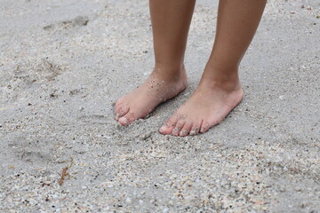 Barefoot child’s feet standing on soft beach sand, capturing a tender and natural moment by the seaside