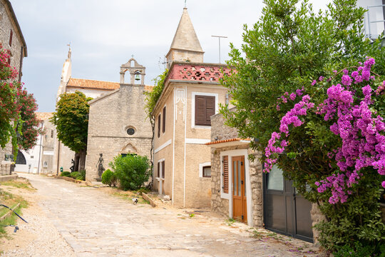 Charming historic street with stone church and blooming bougainvillea in Osor, Croatia