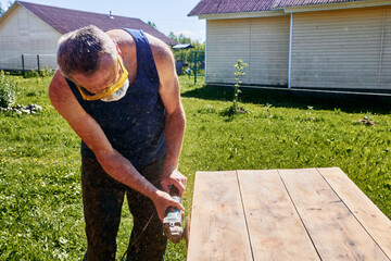 Holding angle grinder with both hands, craftsman wearing respirator and safety glasses sanding tabletop outdoors in rustic countryside setting