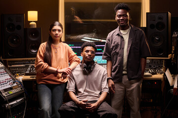 Multiethnic group of young adults standing and sitting in professional recording studio, Black man...