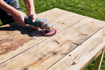 Grinding wood tabletop with handheld angle grinder, sanding disc removing material from surface in...