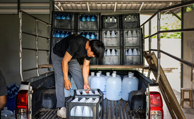 male warehouse worker lifting a bottled drinking water in a crate Load drinking water onto the delivery truck in waterdrink factory, small business