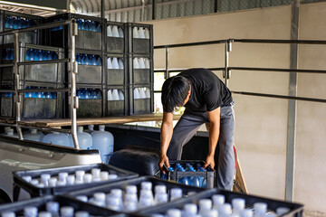 male warehouse worker lifting a bottled drinking water in a crate Load drinking water onto the delivery truck in waterdrink factory, small business