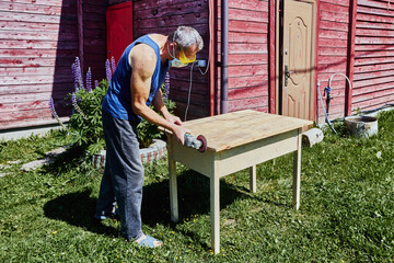 Sanding wooden edge with handheld grinder, carpenter wearing respirator and safety glasses working...