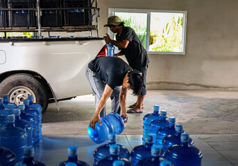 male warehouse worker lifting a Gallon drinking water, Workers transfer drinking water bottles from the production line to trucks in waterdrink factory