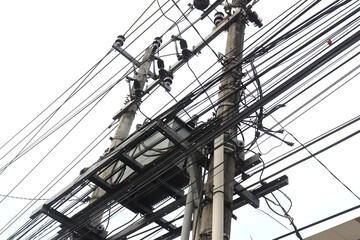 Electric transformer with messy tangled cables set against a sky background. It is part of a...