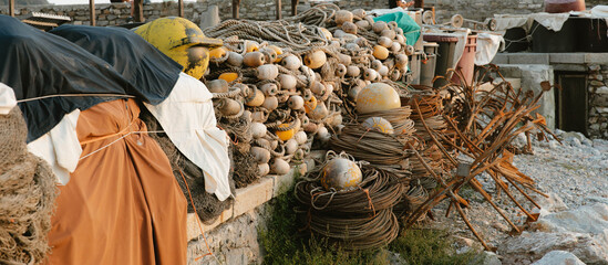 Fishing nets, floats, ropes, and anchors resting on stone wall at harbor