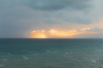 Obraz premium Golden sunset illuminating calm ocean under cloudy sky