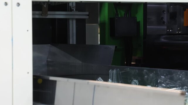 PET bottle preforms line. Plastic bottle preforms on conveyor belt in automated manufacturing system. Industrial injection molding and high speed production in a modern plastic packaging PET factory.