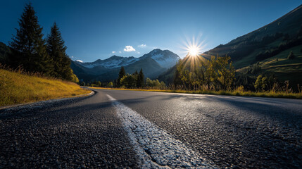 Foothills of the Austrian Alps with asphalt road on foreground and sun on blue morning sky