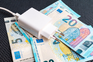 Phone charger white electric power plug on the Euro paper money. Electricity cost, savings concept.
