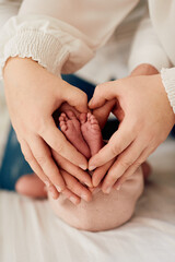A close up of parents hands forming a heart around their newborns tiny feet, symbolizing love,...