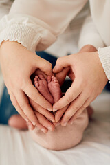 A close up of parents hands forming a heart around their newborns tiny feet, symbolizing love,...