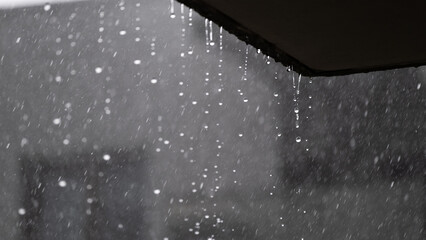 Heavy rain falling from building roof with blurred urban background
