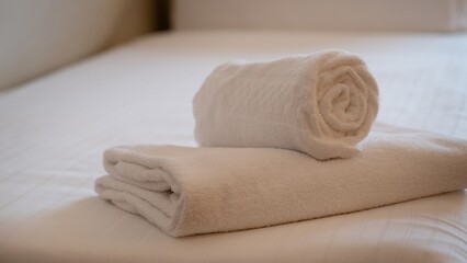 Rolled and folded white towels on neatly made bed