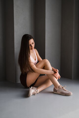 Teenage girl brunette in stylish clothes posing in sitting pose against gray wall